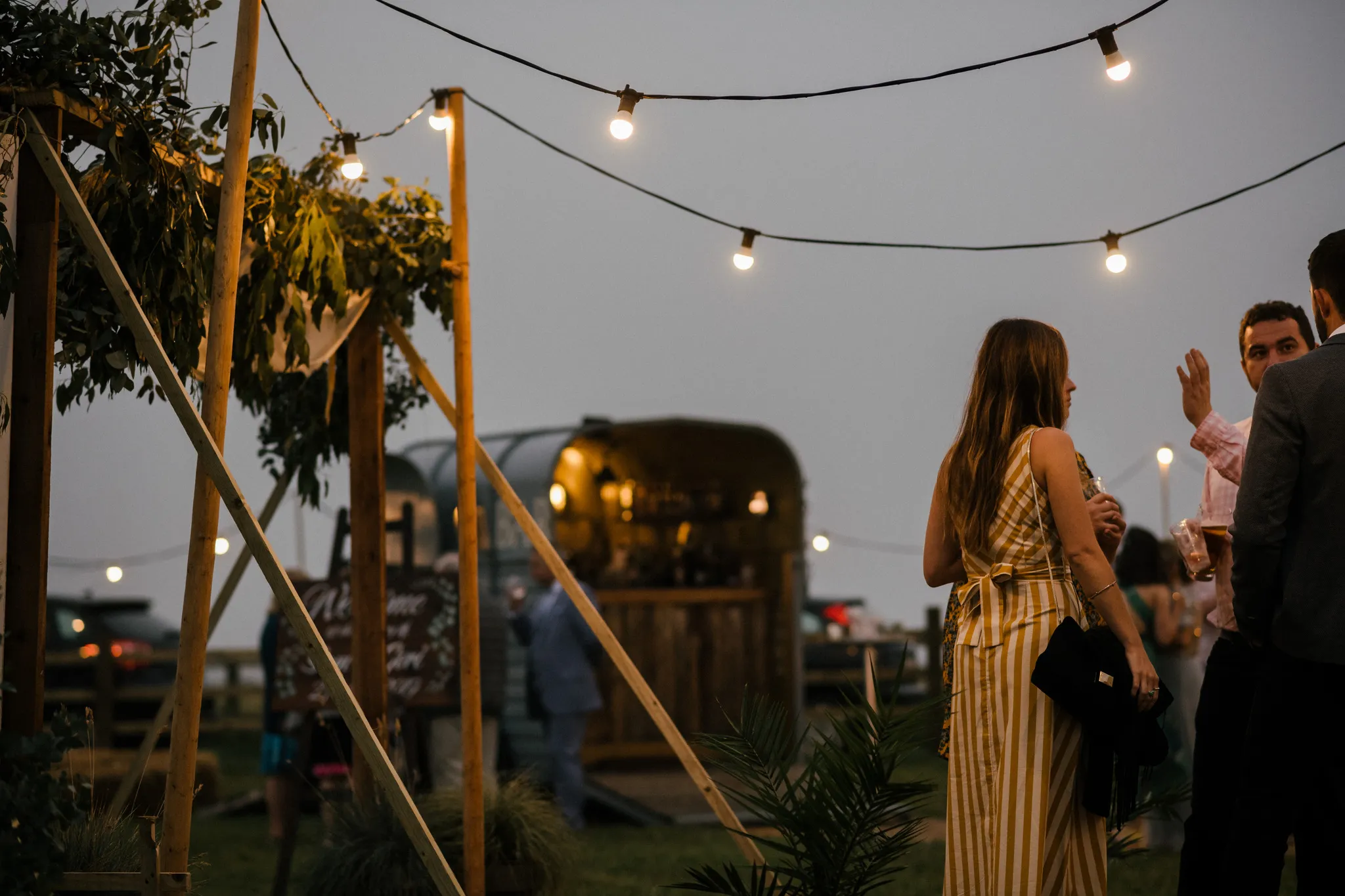 Wedding guests at dusk with horsebox bar and fairy lights at a Yorkshire venue