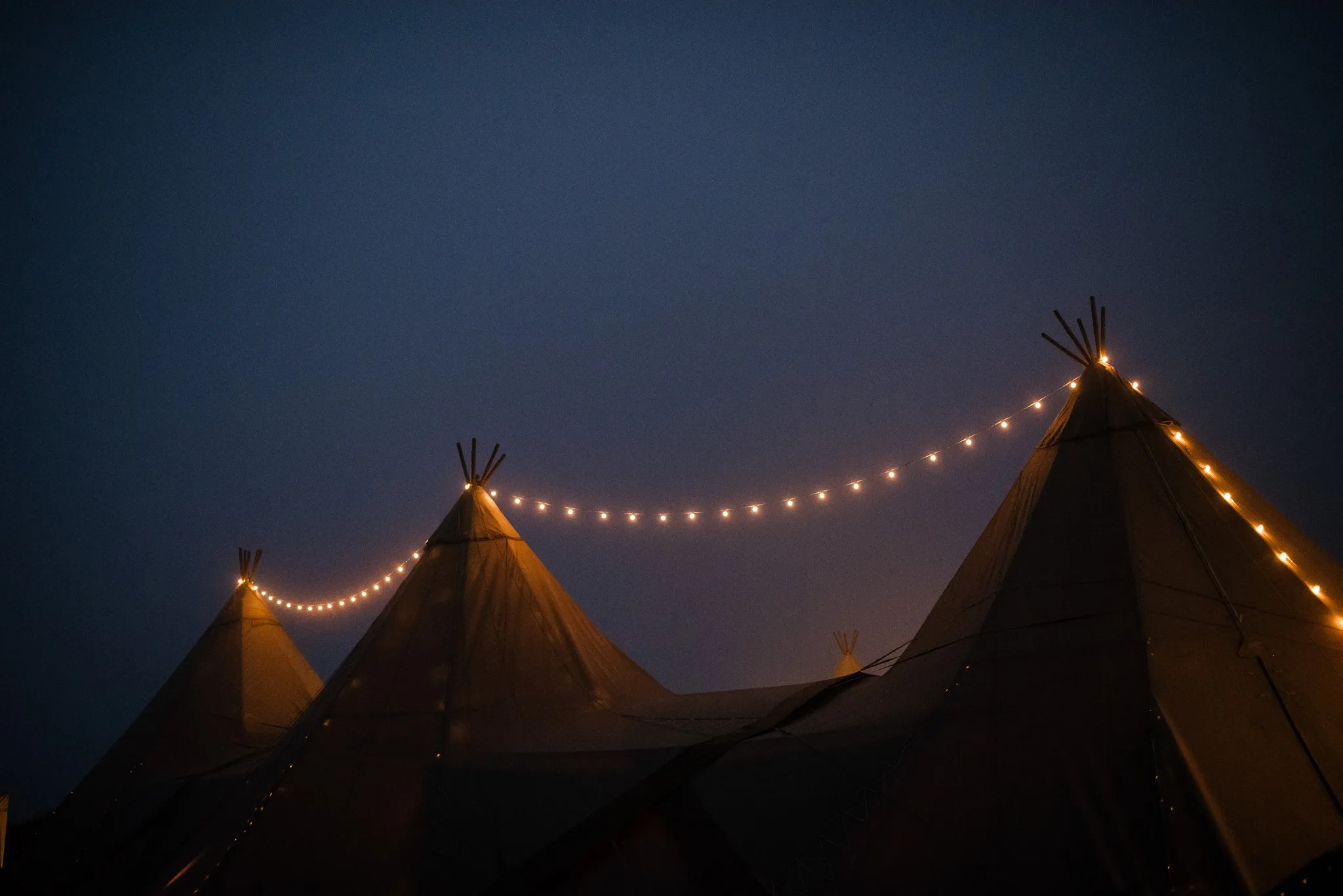 Three tipis lit up at night at a Yorkshire wedding